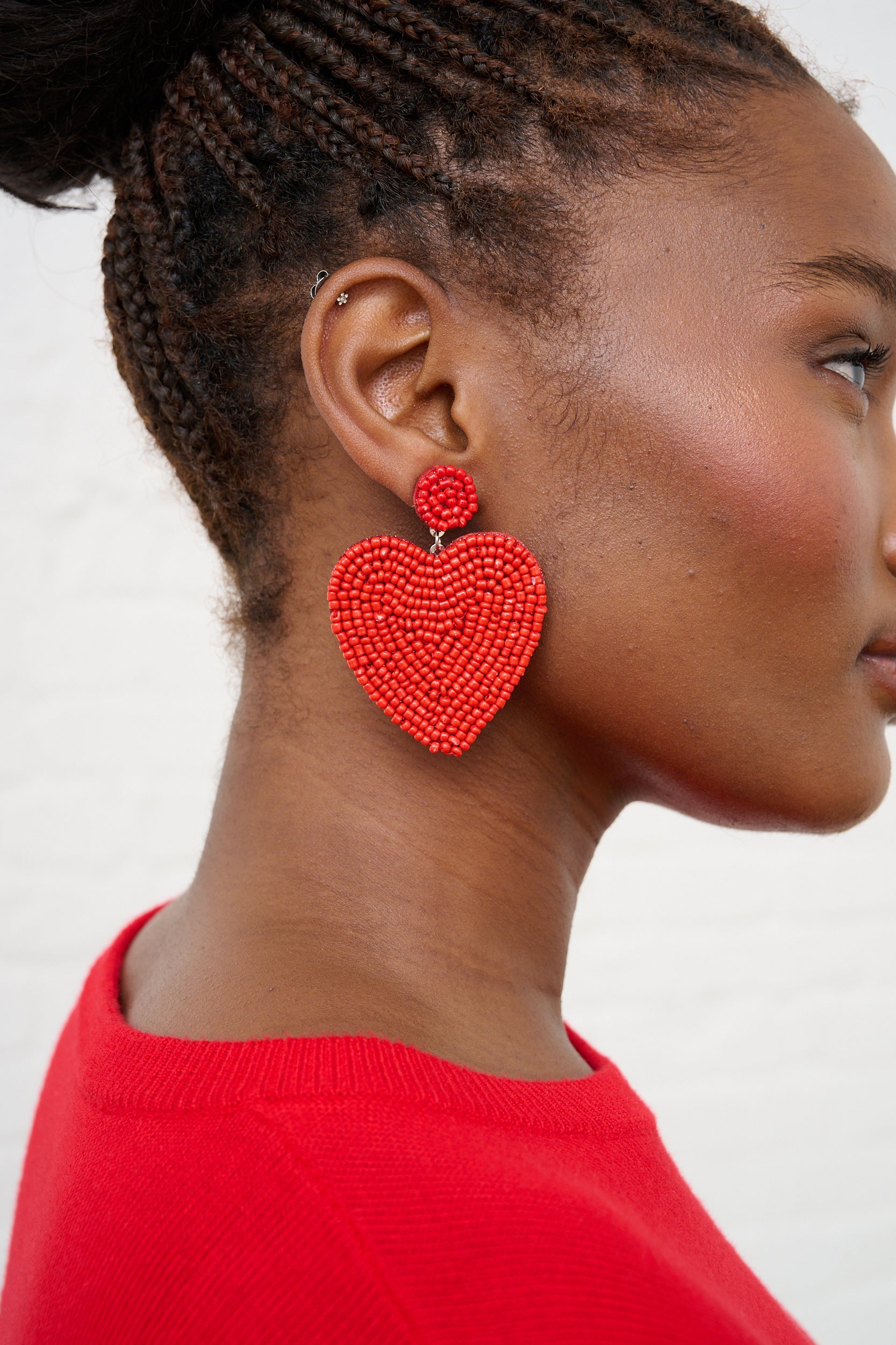 Model is wearing red heart earrings with a red sweater 