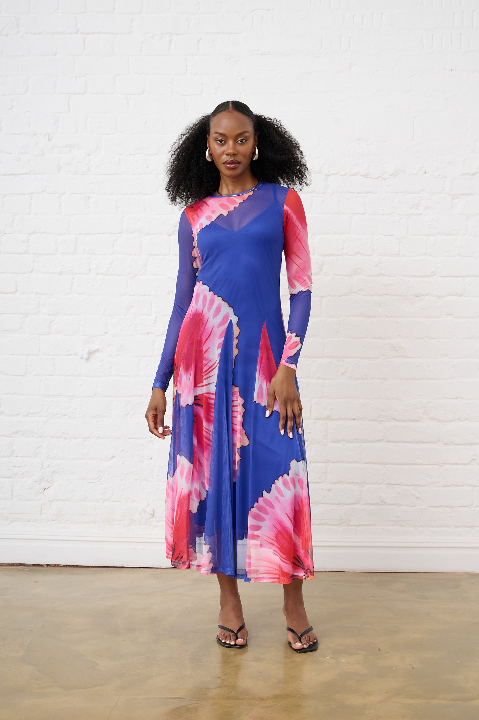 Model is wearing a blue and pink long sleeve maxi dress with black heels and silver earrings 