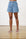 Model is wearing medium wash denim shorts with white flip flops
