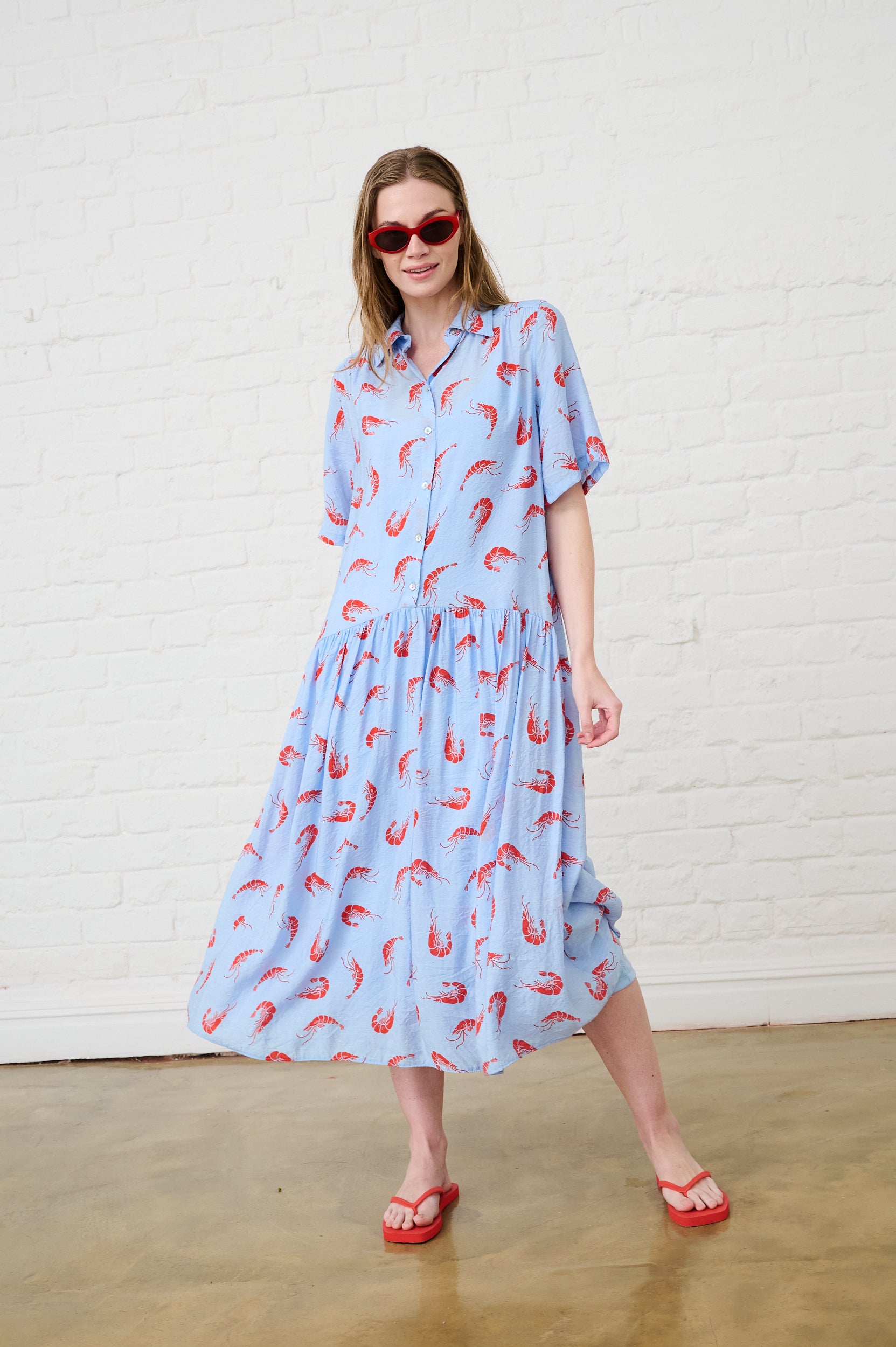 Model is wearing a blue dress with orange prawns on it and red slops