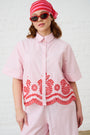 Model is wearing and pink and red stripe top with detailed hem, red sunglasses