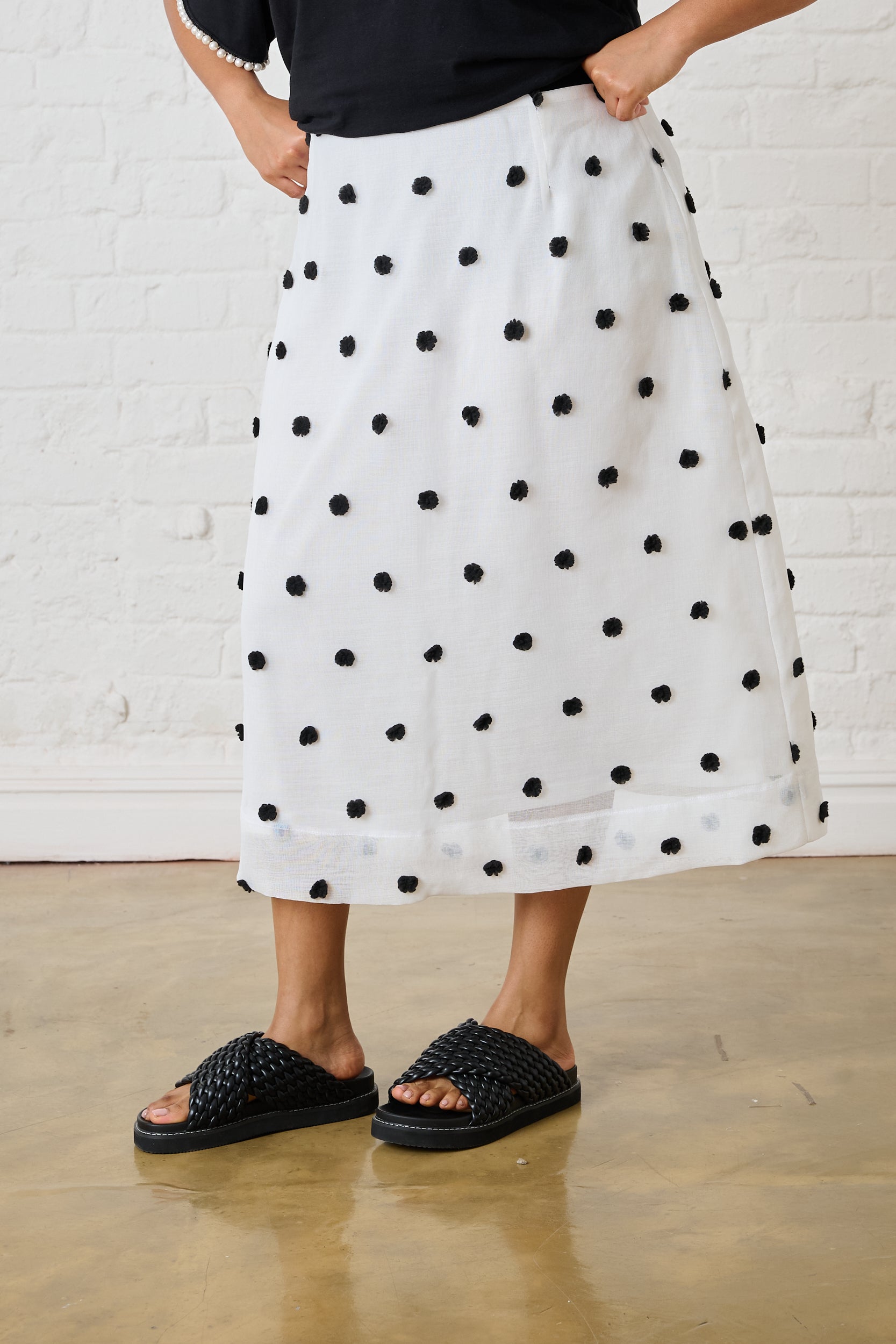 Model is wearing a black and white spotted skirt with black sandals 