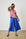 Model is wearing blue linen pants with a floral top and blue sandals