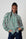 Model is wearing a green and pink stripe bellow sleeve shirt with blue denim jeans 