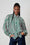 Model is wearing a green and pink stripe bellow sleeve shirt with blue denim jeans 