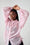 Person wearing a light pink shirt with long sleeves against a white brick wall.