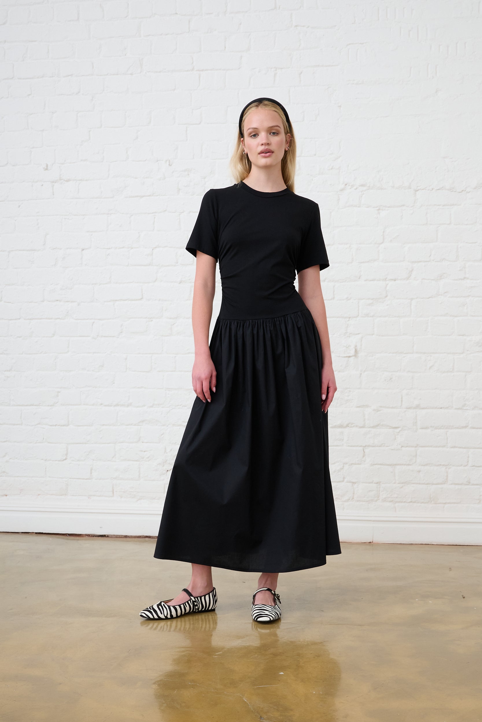 Model is wearing a black short sleeve combo dress with white and black ballet flats 