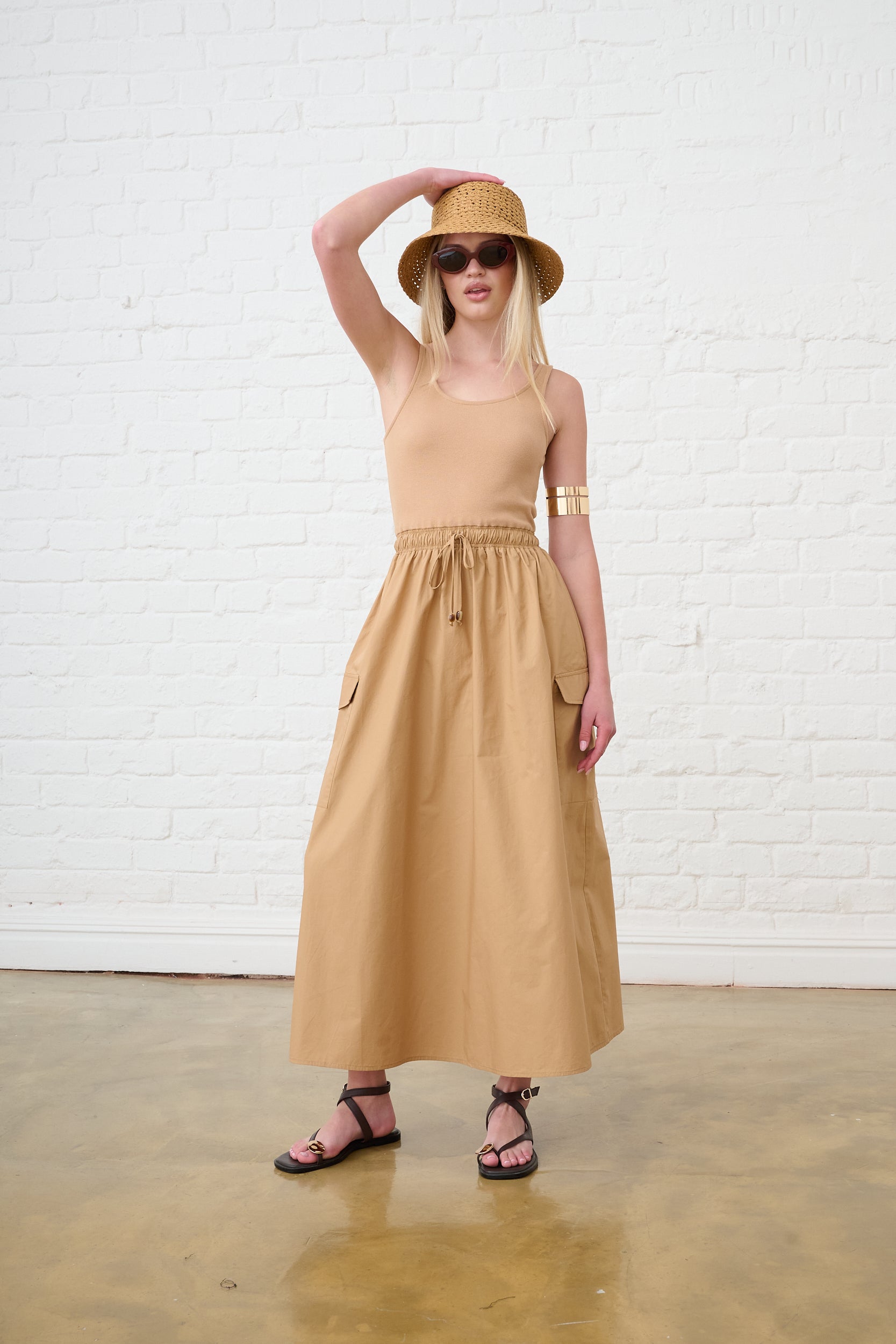 Model is waring a utility dress with pockets in a natural brown colour and brown sandals