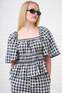 Model is wearing a black and white gingham check short sleeve top with black sunglasses