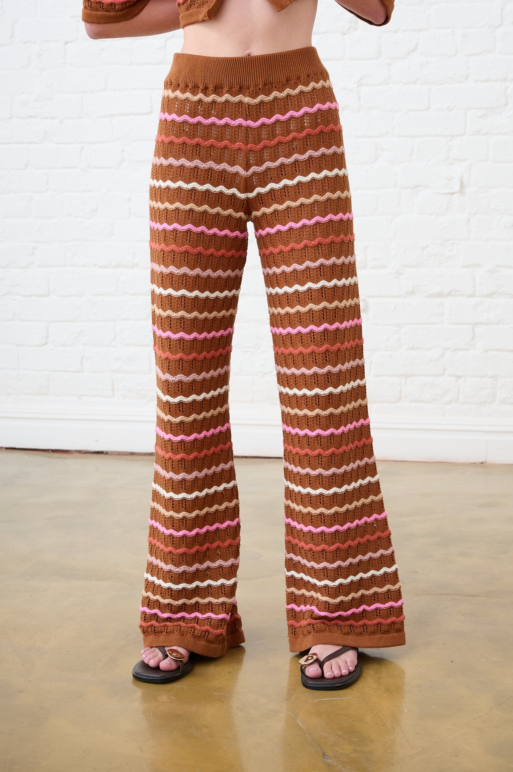 Model is wearing multi-colour stripe crochet pants with brown sandals