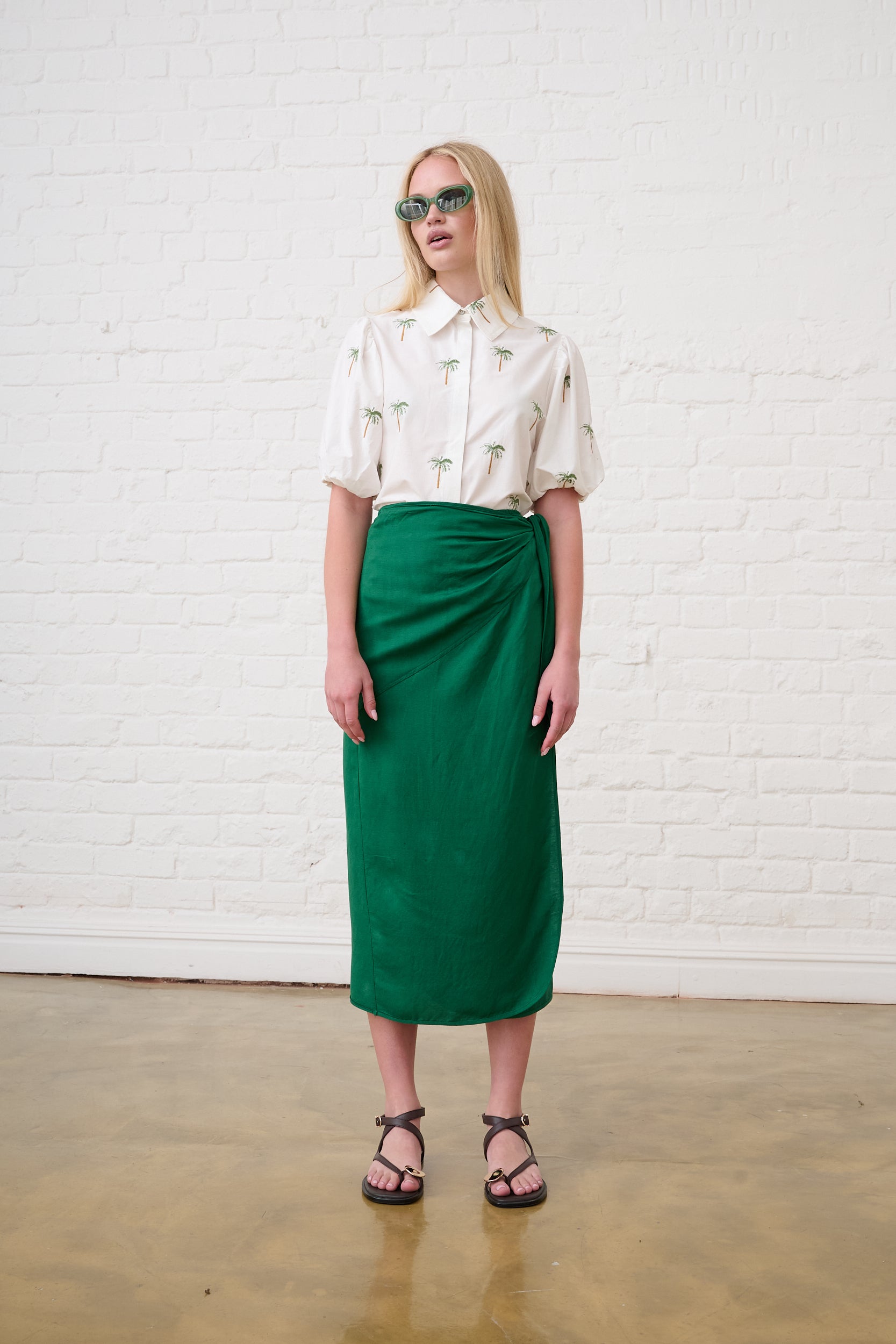 Model is wearing a green linen wrap skirt and a white blouse with brown sandals