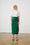 Model is wearing a green linen wrap skirt and a white blouse with brown sandals