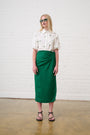 Model is wearing a green linen wrap skirt and a white blouse with brown sandals