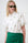 Model is wearing a white puffed sleeve shirt with embroidered palm trees on and a green wrap skirt 