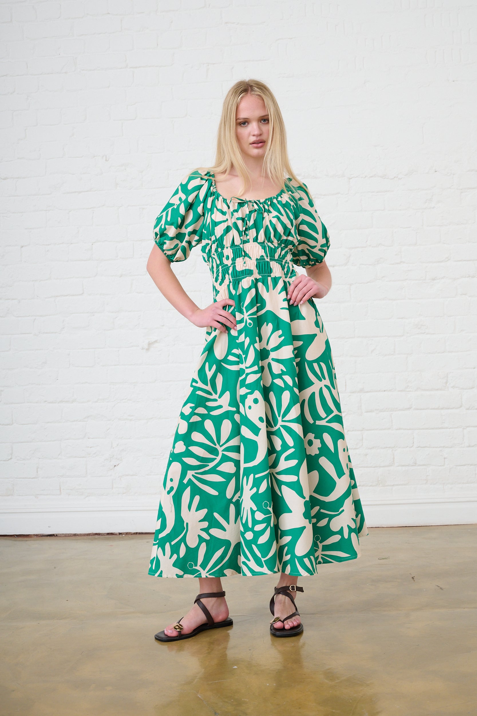 Model is wearing a green print maxi length dress and brown sandals 