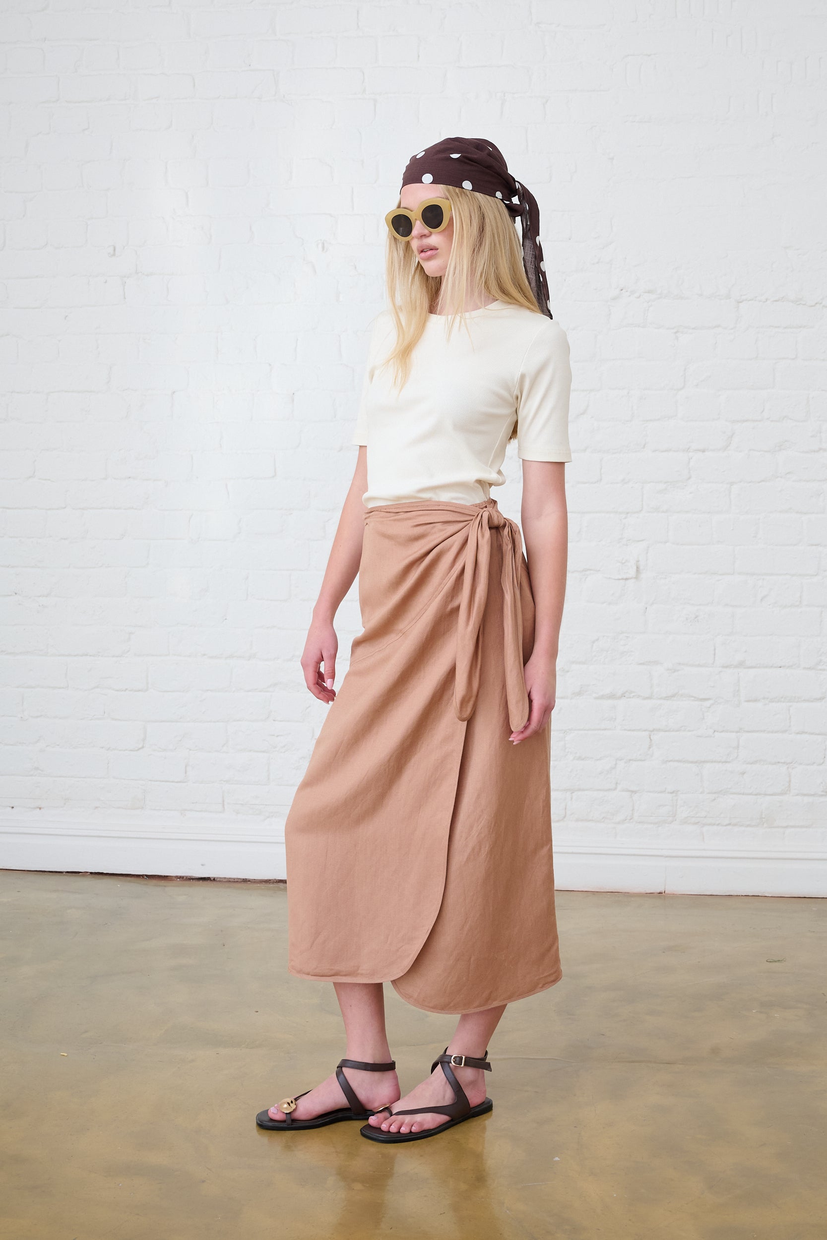 Model is wearing a brown linen wrap skirt with a cream top and brown sandals