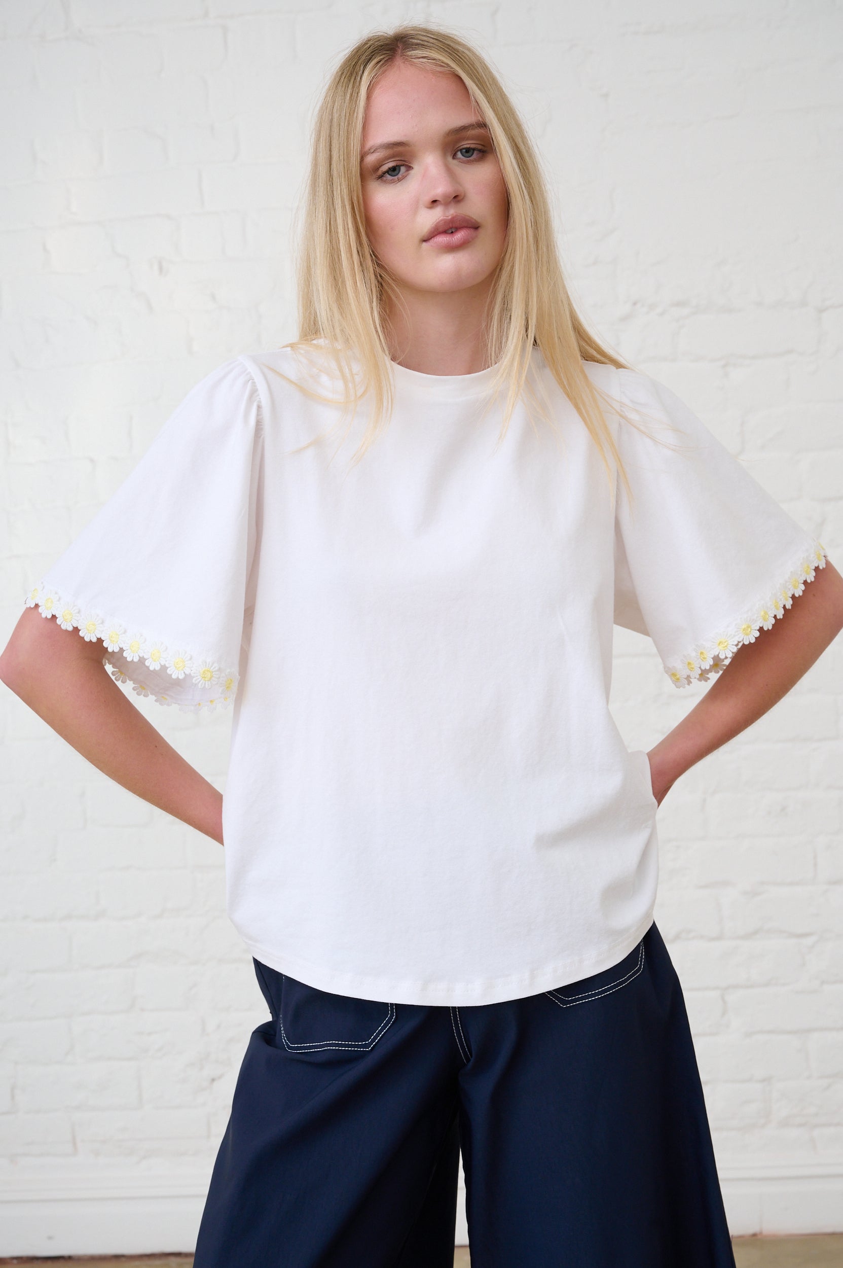 Model is wearing a white T-Shirt with yellow daisy trim and navy pants