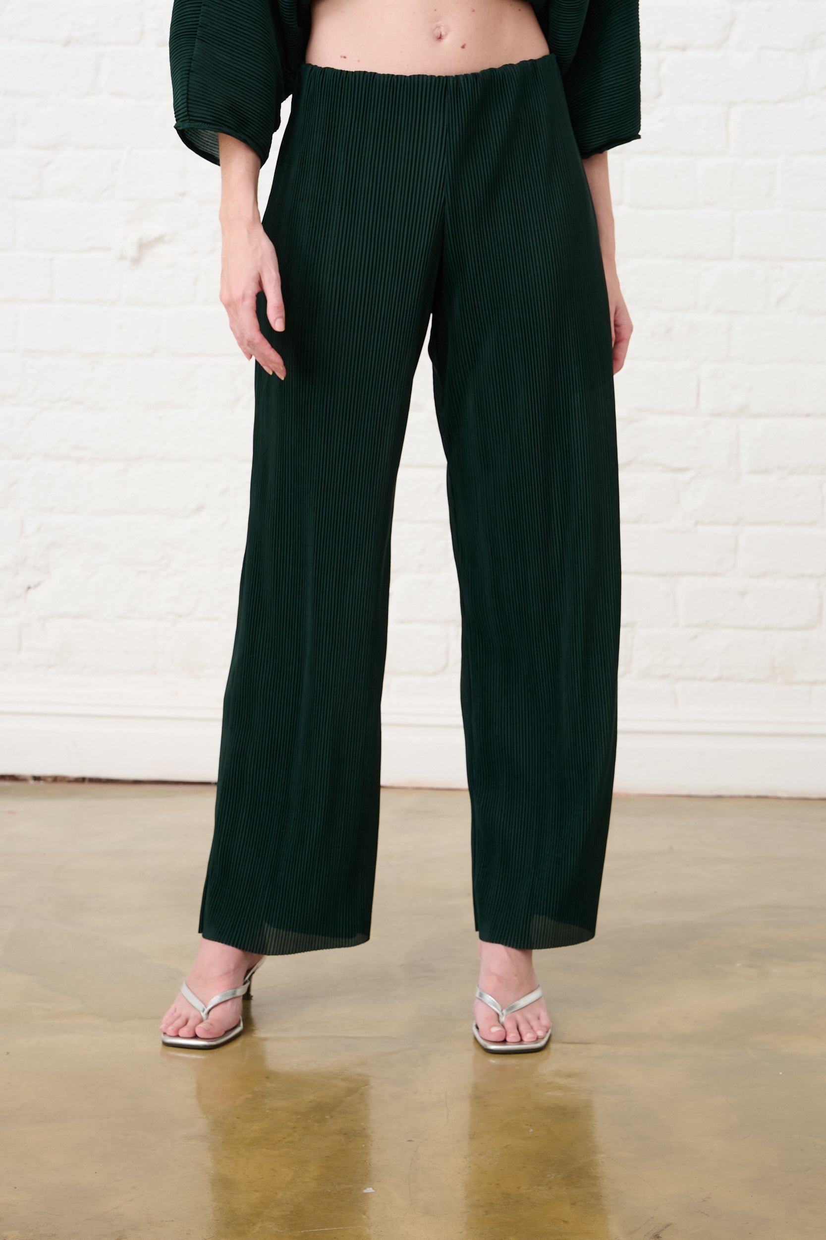 Model is wearing bottle green pull of pants with silver heels and a matching green top