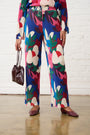 Model is wearing multicolour floral pants with a burgundy bag and shoes 