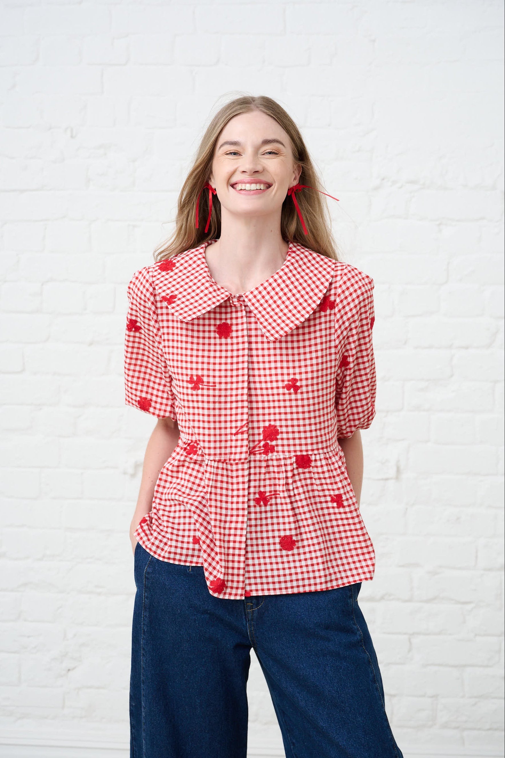 Model is wearing a red and white gingham blouse with dark blue jeans.