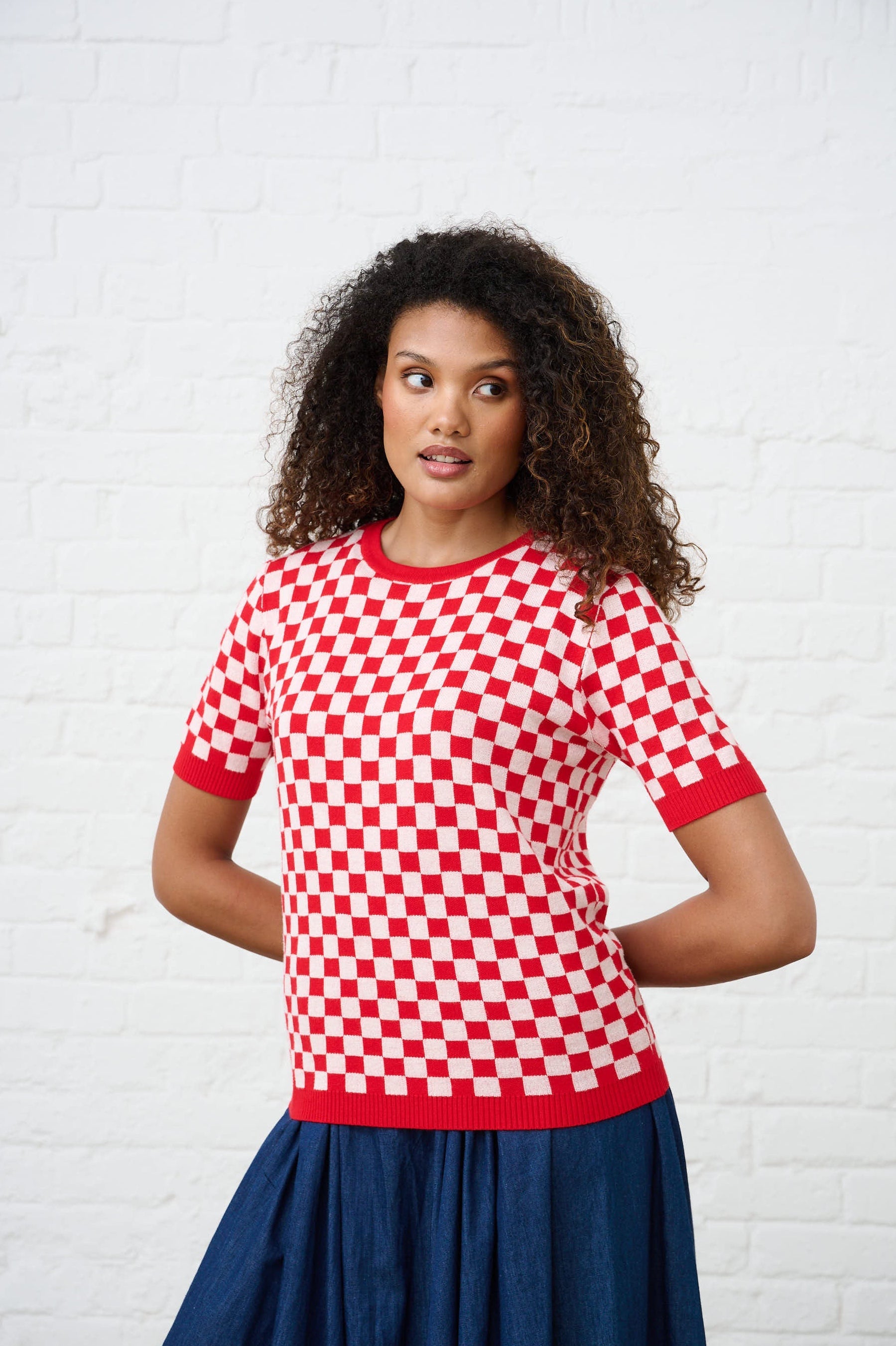 model is wearing a red and white check sweater with a denim skirt