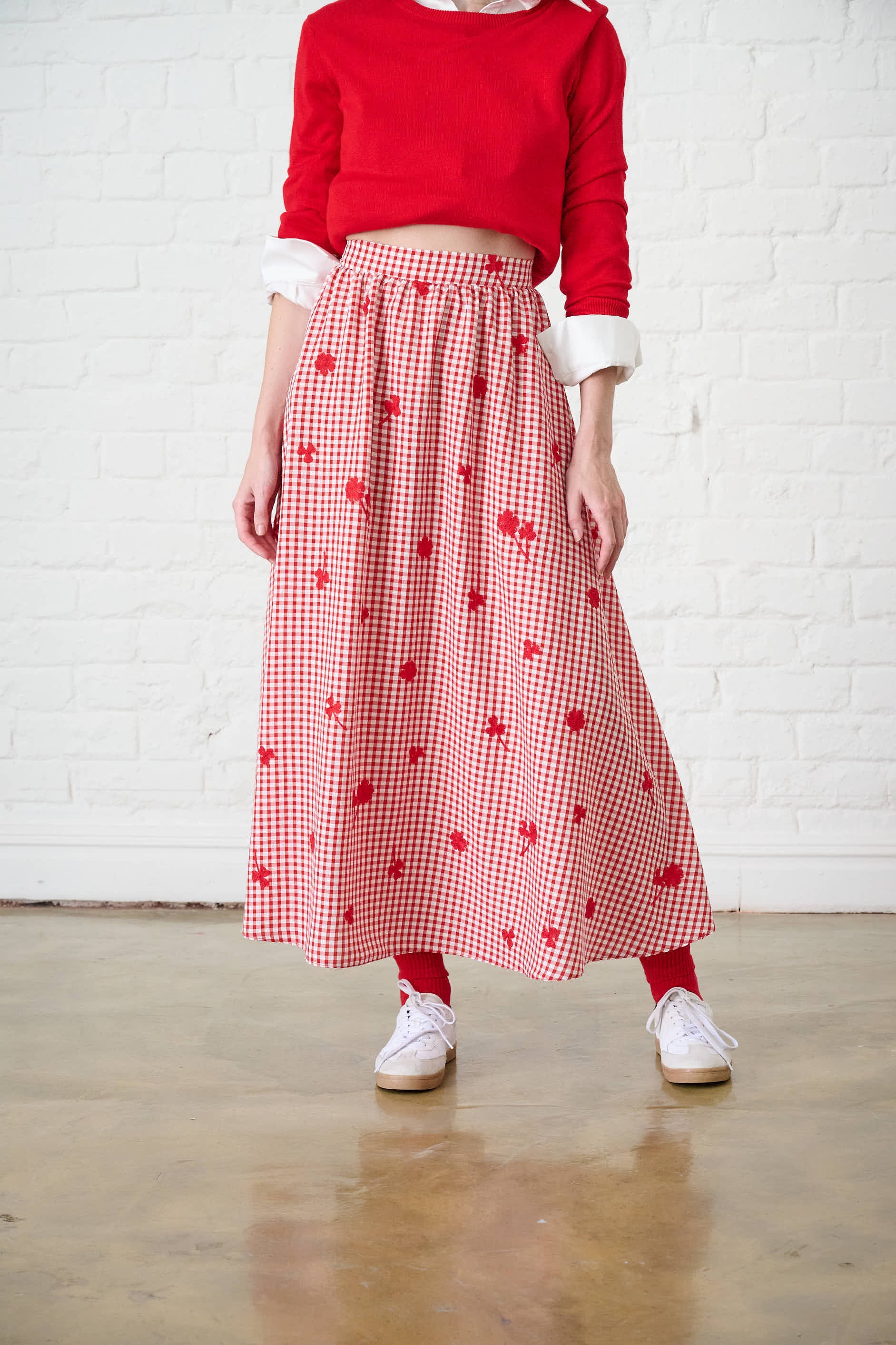 Model is wearing a red Gingham Skirt with a red sweater and white sneakers
