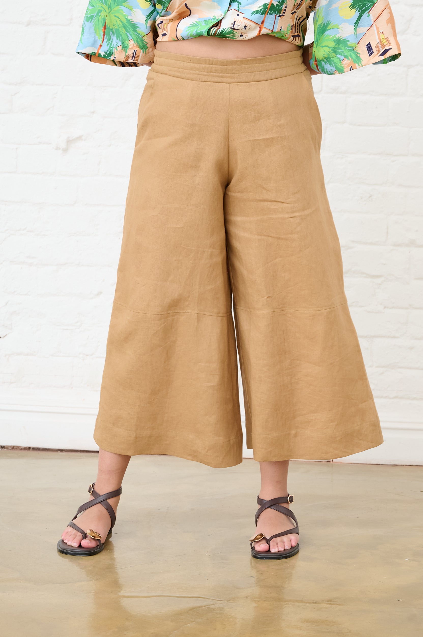 Model is wearing wide leg brown linen pants with brown sandals