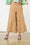 Model is wearing wide leg brown linen pants with brown sandals