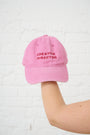 Pink cap with 'CREATIVE DIRECTOR' text held by a person on a light pink background