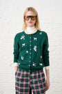 Model is wearing a green cardigan with bows and flower details with pink and green check pants 