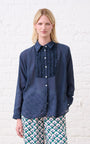 Model is wearing a blue frill shirt with pie crust detail and pink and green patterned pants, with black loafers