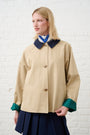 Model is wearing a cropped trench oat in tan with a green gingham lining, and a navy skirt