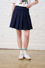 Model is wearing a navy blue pleated skirt with white sneakers and a white tee