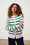 Model is wearing a pastel striped cardigan with dark wash jeans 