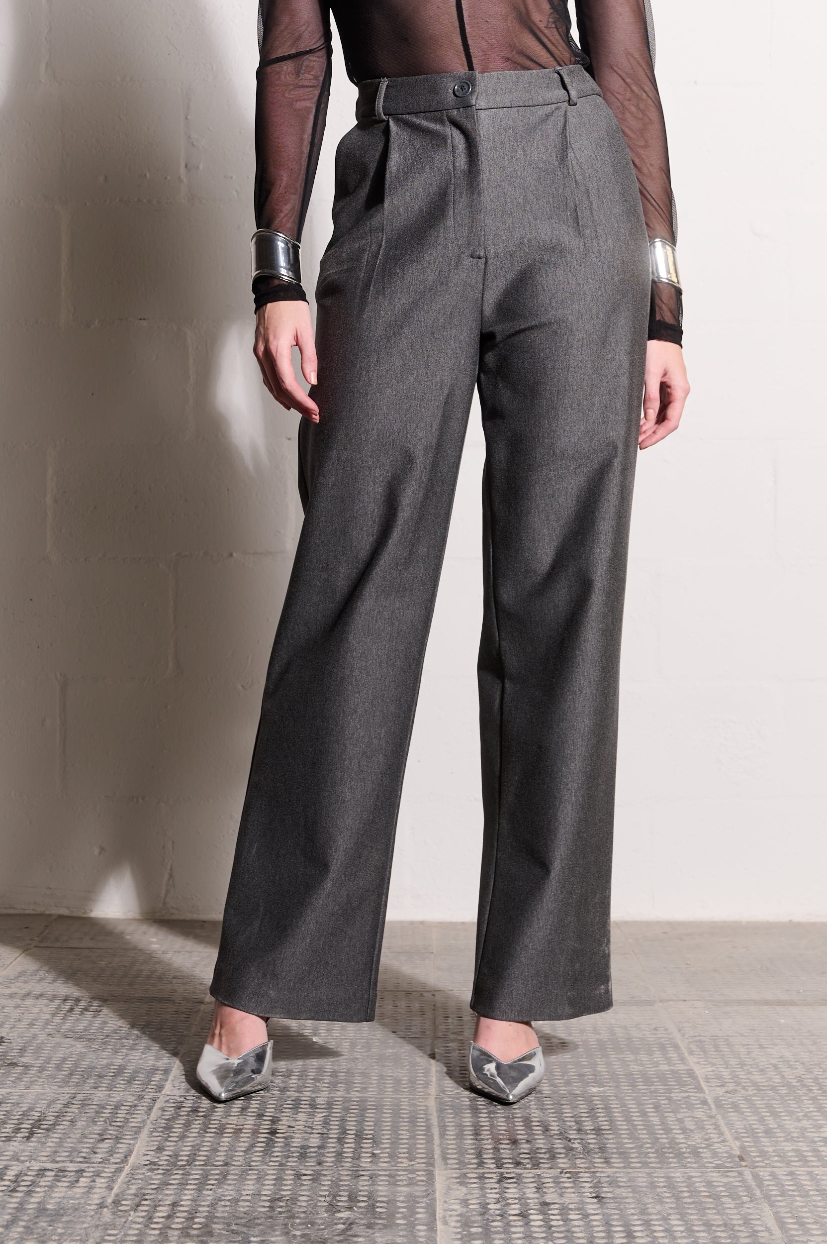Model is wearing grey pants, a black mesh top and silver shoes