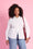 Model is wearing white long sleeve button up with denim jeans and a red bag 