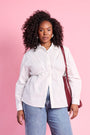 Model is wearing white long sleeve button up with denim jeans and a red bag 