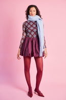 Model is wearing a burgundy bubble mini skirt with burgundy tights, a mesh top and a blue scarf