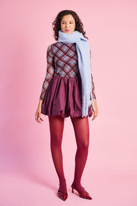 Model is wearing a burgundy bubble mini skirt with burgundy tights, a mesh top and a blue scarf