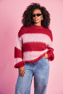 Model is wearing a burgundy and pink striped knitted jumper with blue denim jeans 