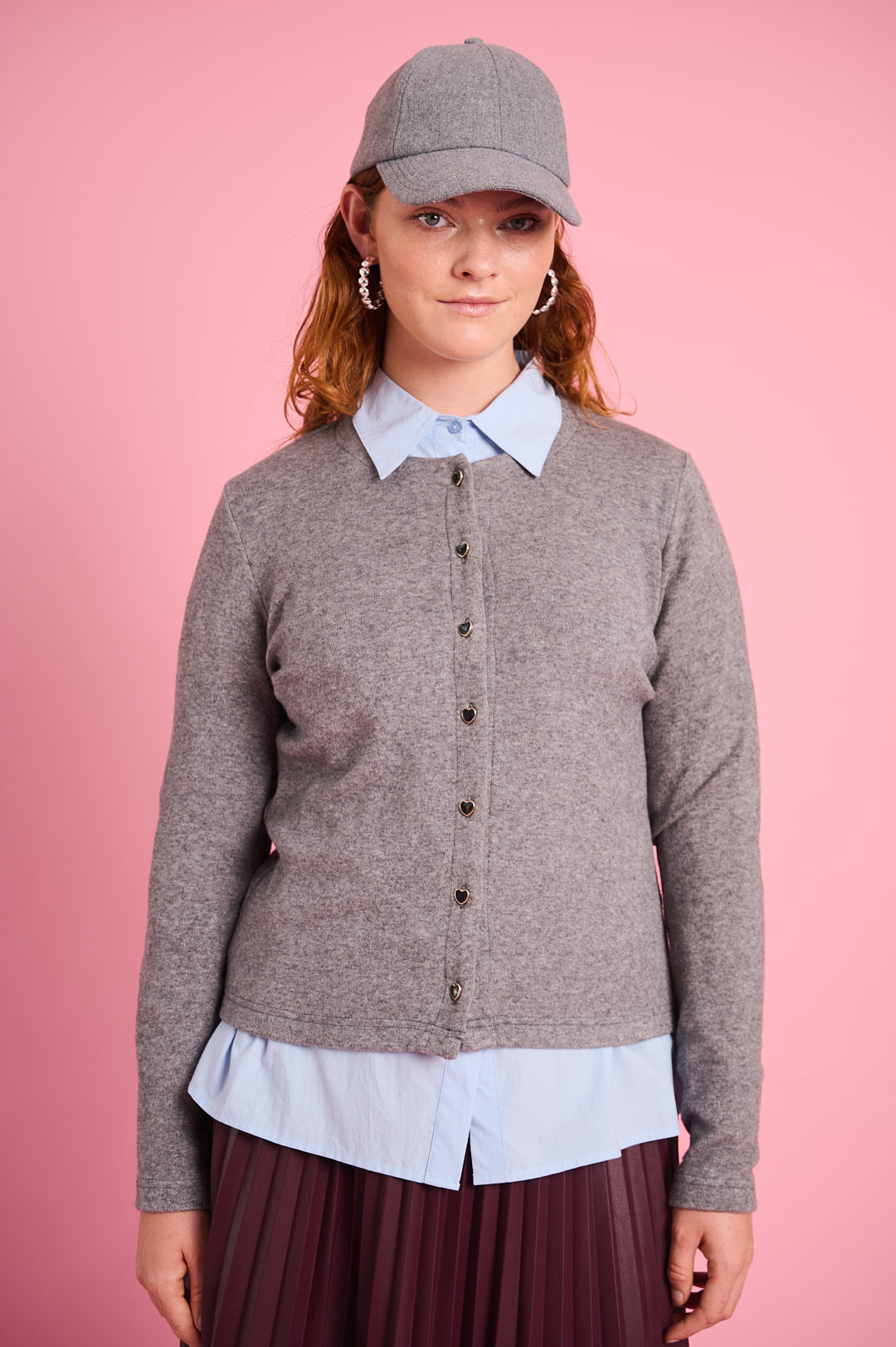 Model is wearing a grey cardigan with black heart buttons and a burgundy skirt with  grey cap