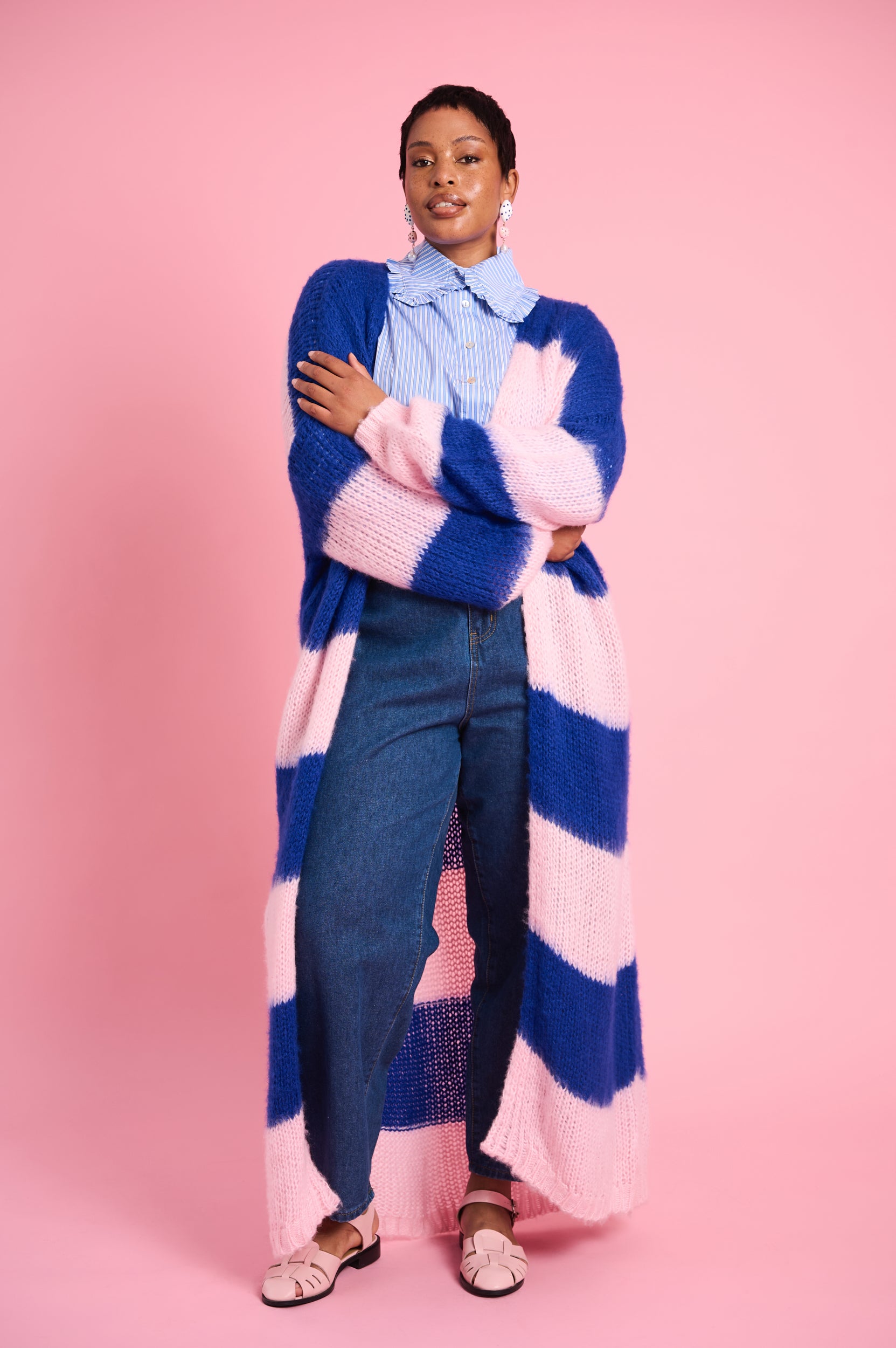 Model is wearing blue and pink striped cardigan with blue jeans and pink shoes 