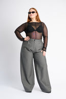 Person wearing a black sheer top and gray wide-leg pants on a white background