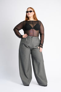 Person wearing a black sheer top and gray wide-leg pants on a white background