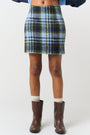 Model is wearing a green and blue melton check skirt with brown boots 