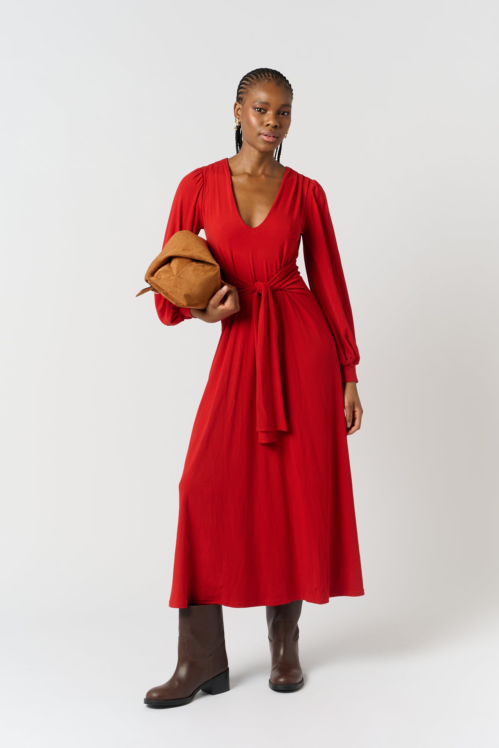Model is wearing a red maxi dress with brown ankle boots and a brown bag