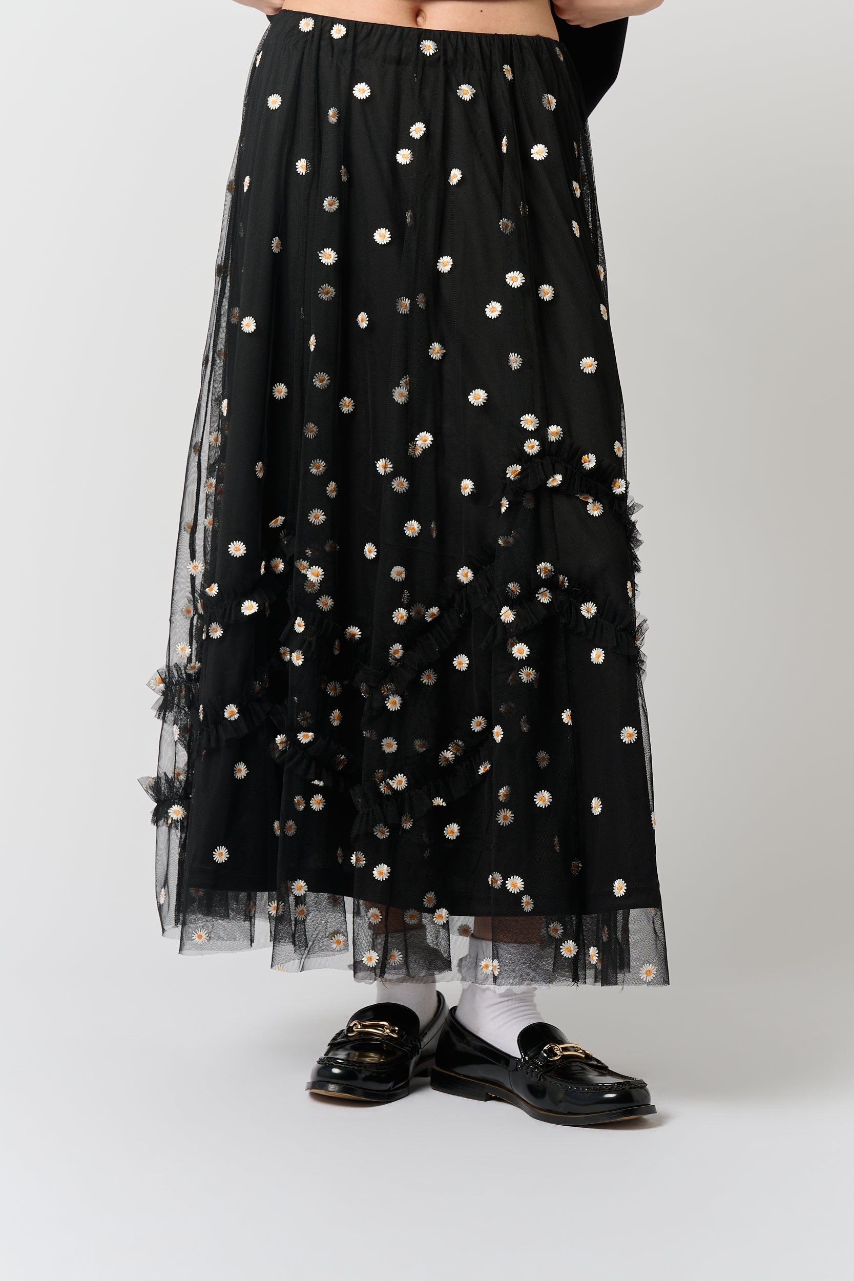 Model is wearing a black skirt with daisy embroidery and black shoes