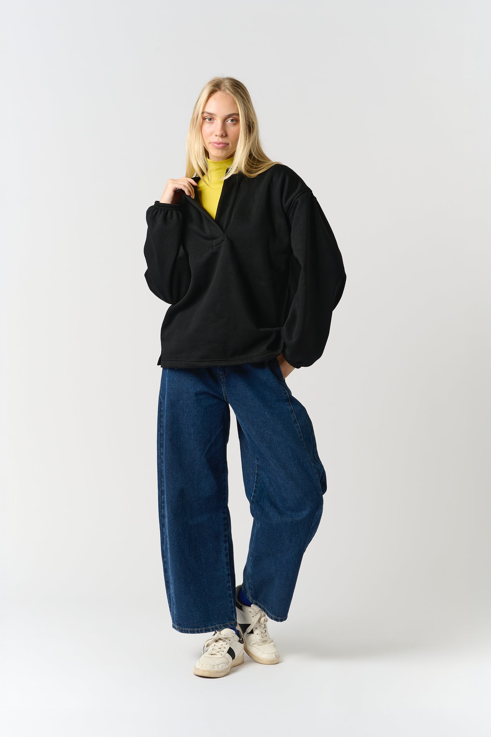 Model is wering a black sweatshirt with a v neck detail, with a lime polo neck and blue denim jeans