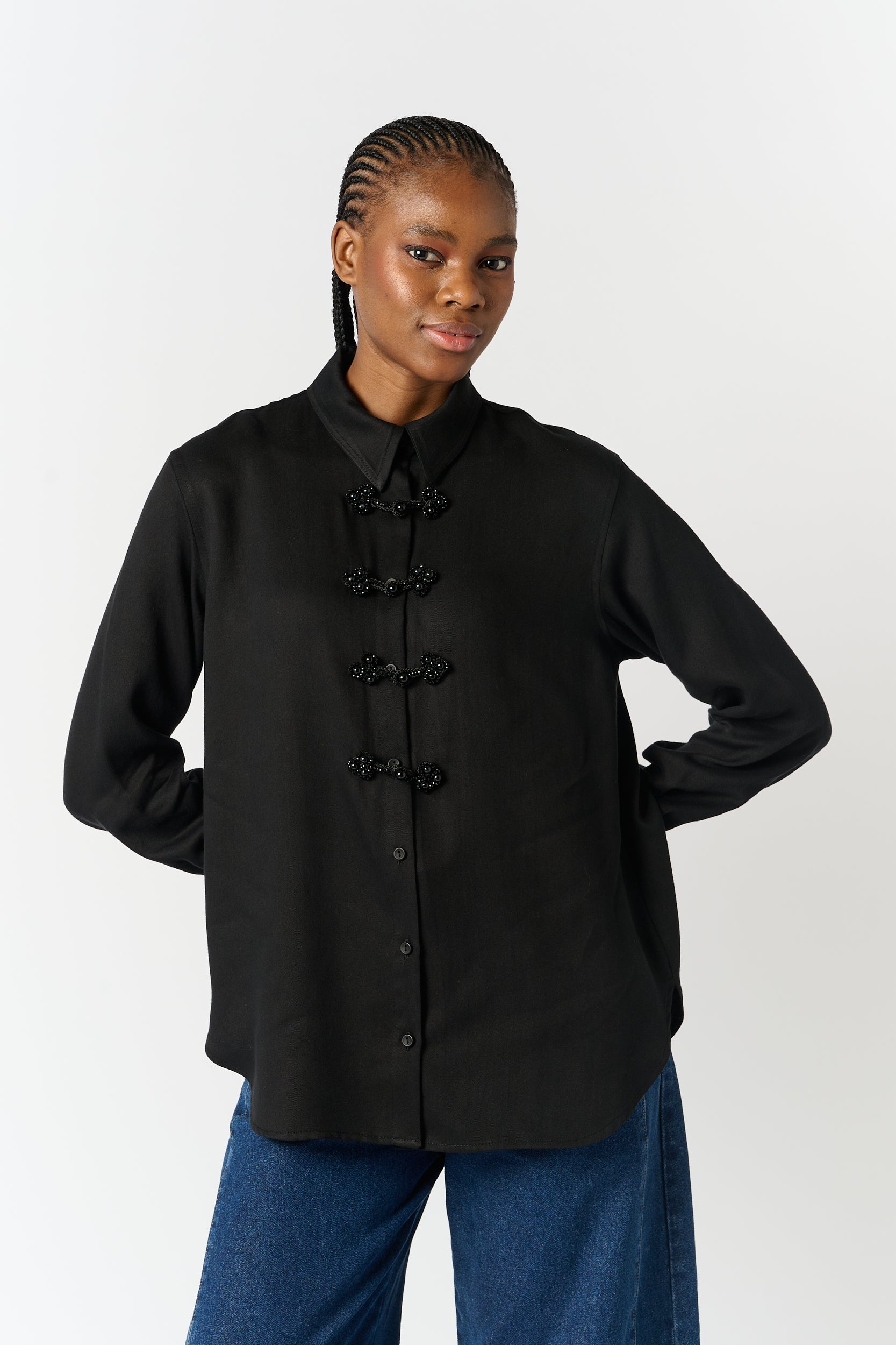 Model is wearing a black shirt with beaded closures and blue denim jeans 