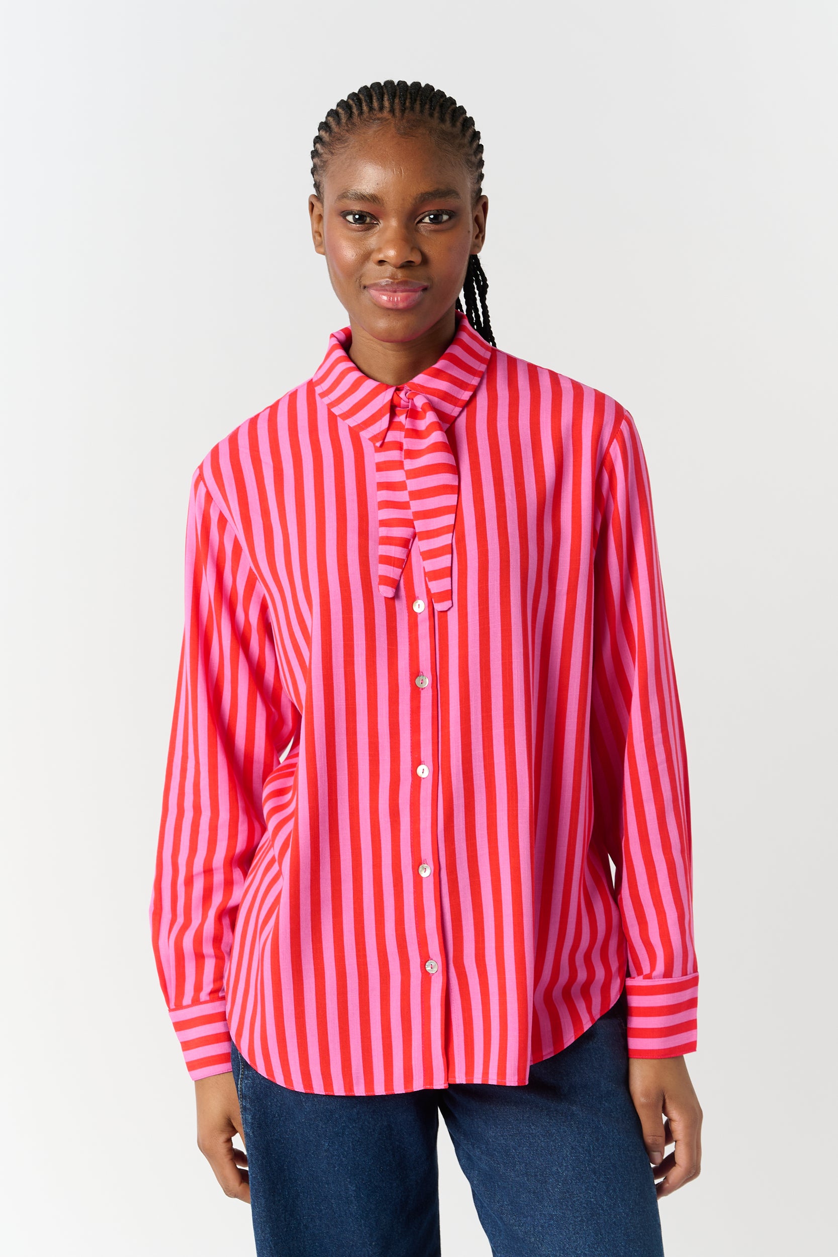Model is wearing a pink and red striped button down shirt with a scarf tie detail 